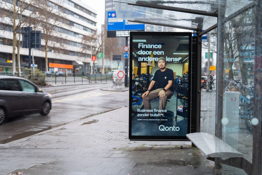 Digitale Qonto-abri met fietsenmaker in beeld naast een natte weg in Rotterdam