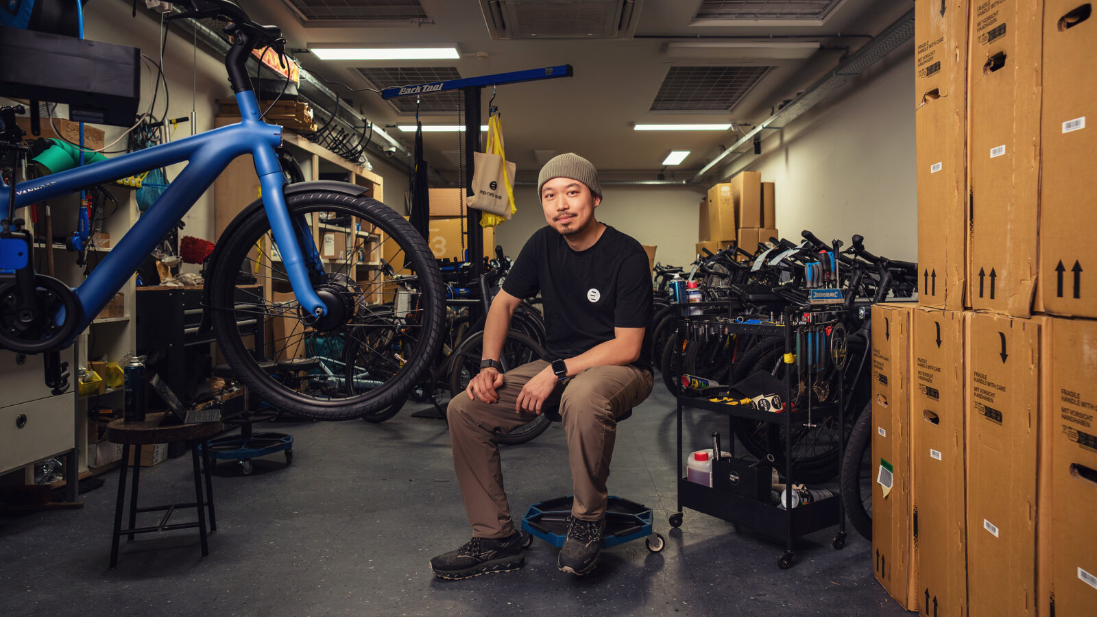 Fietsenmaker met muts zit in zijn werkplaats tussen de fietsen en gereedschapskarren