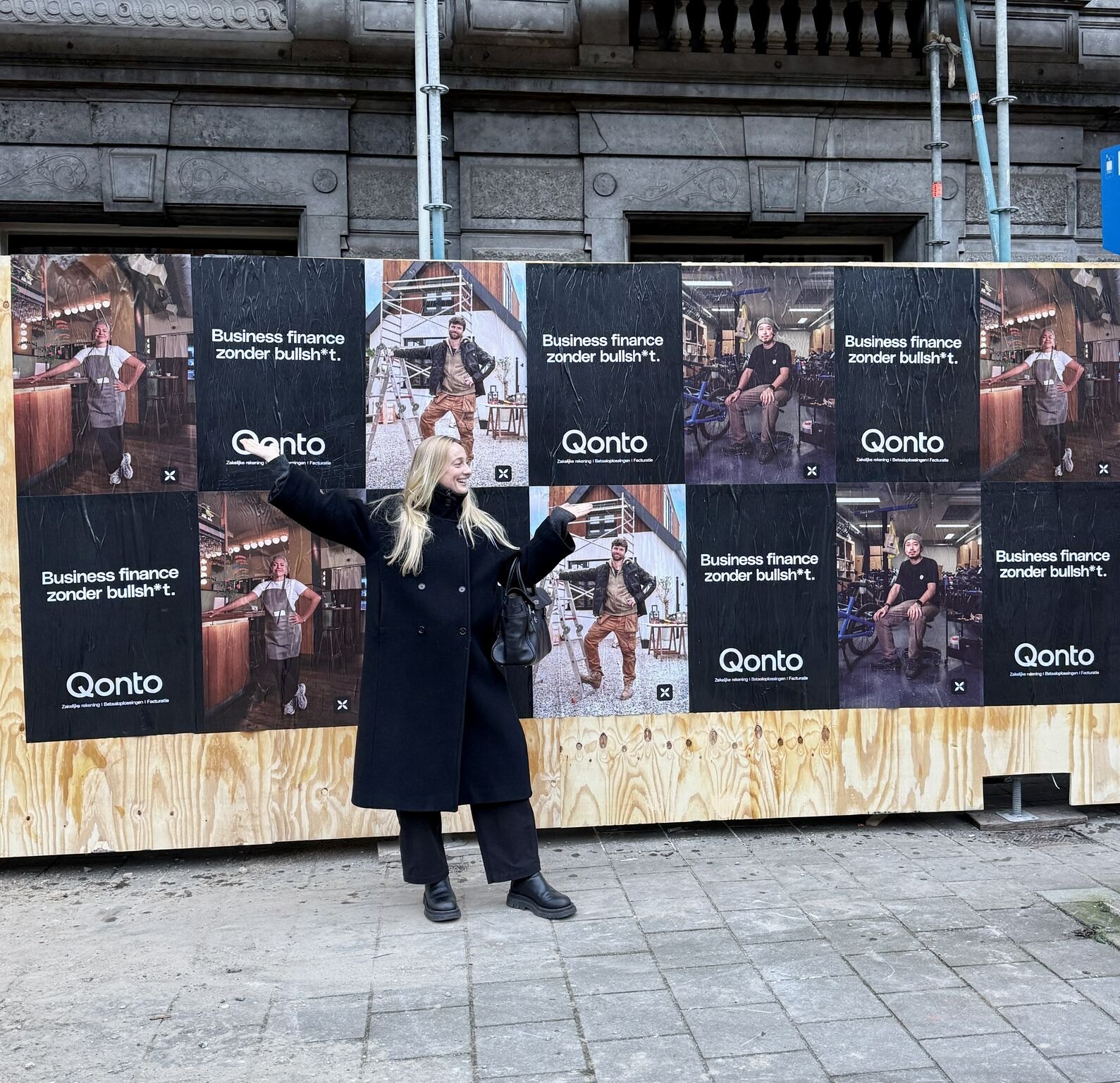 Vrouw poseert voor een bouwschutting vol Qonto-posters in Amsterdam