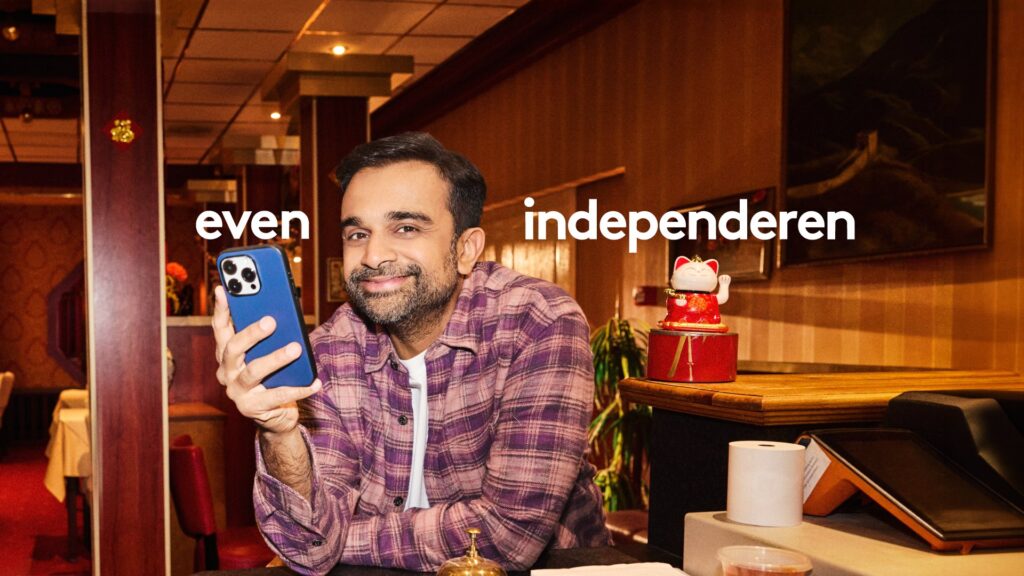 Restaurant owner holding his phone next to a waving lucky cat in the Independer Why not now campaign by Wolfstreet